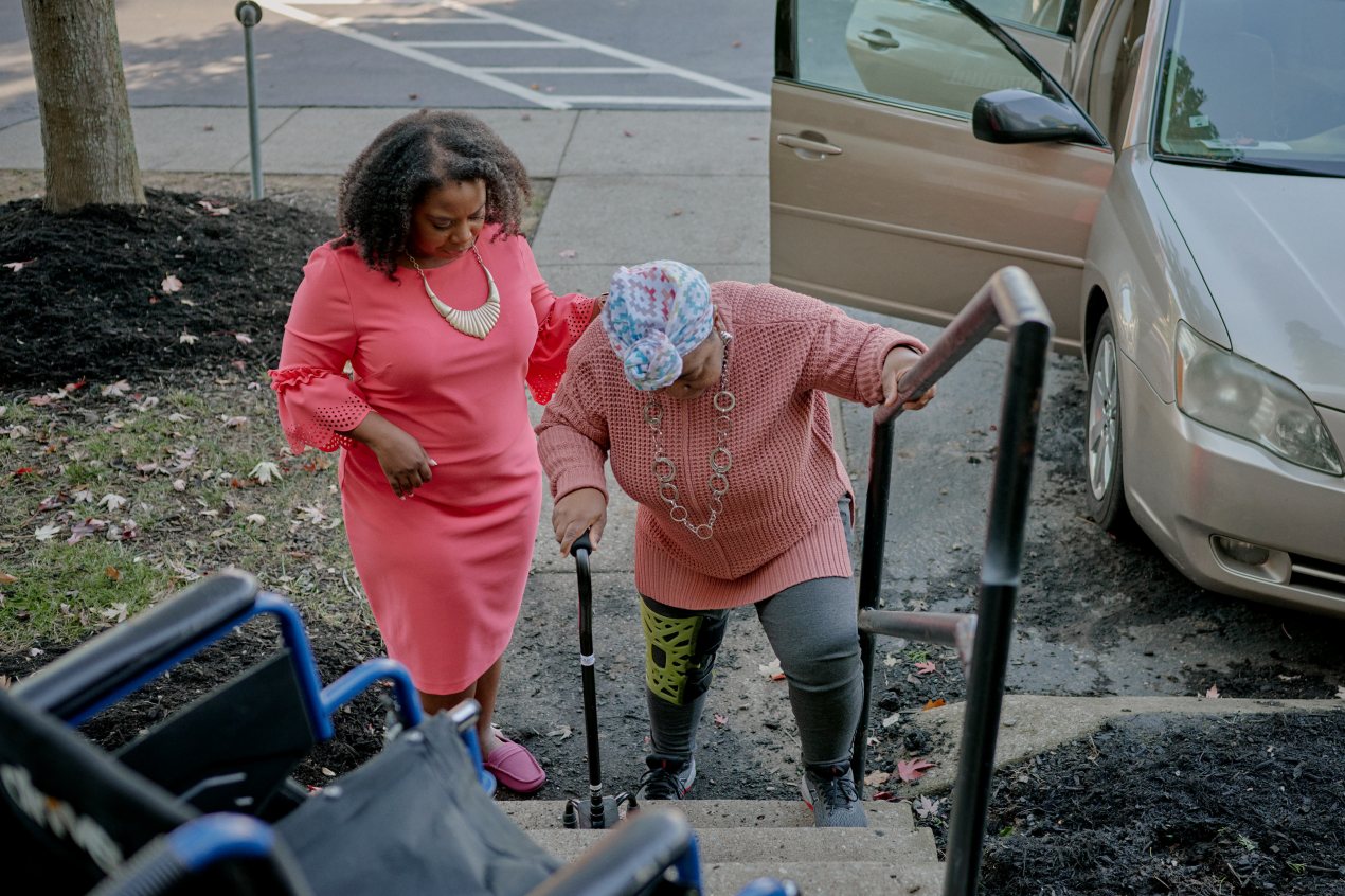 A photo of a woman helping her elderly mother up the stairs.