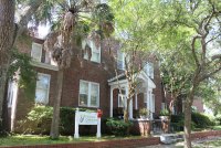 An old brick building with a white sign in front reading "Florence Crittenton Programs of SC" and surrounded by trees.
