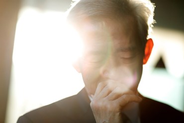 A photo of an elderly man looking fatigued in front of a window.