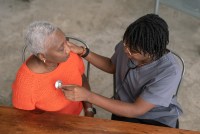 A young nurse wearing medical scrubs checks a senior patients heart rate.