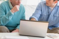 A photo of an older man receiving computer help from a younger man.