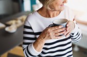 A photo of an older woman holding a mug inside her house.