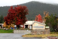A yellow sign with blue lettering says "Intermountain, restoring hope for children" outside a building in Helena, Montana. A bright red tree and a playground can be seen in the background next to the building.