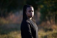 A woman stands outside in late afternoon sun and looks at the camera.