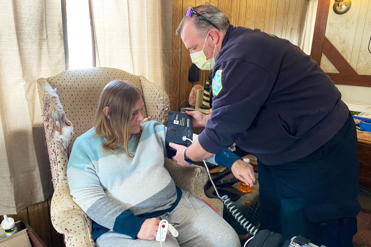 A photo of a male paramedic taking a woman's blood pressure in her home.